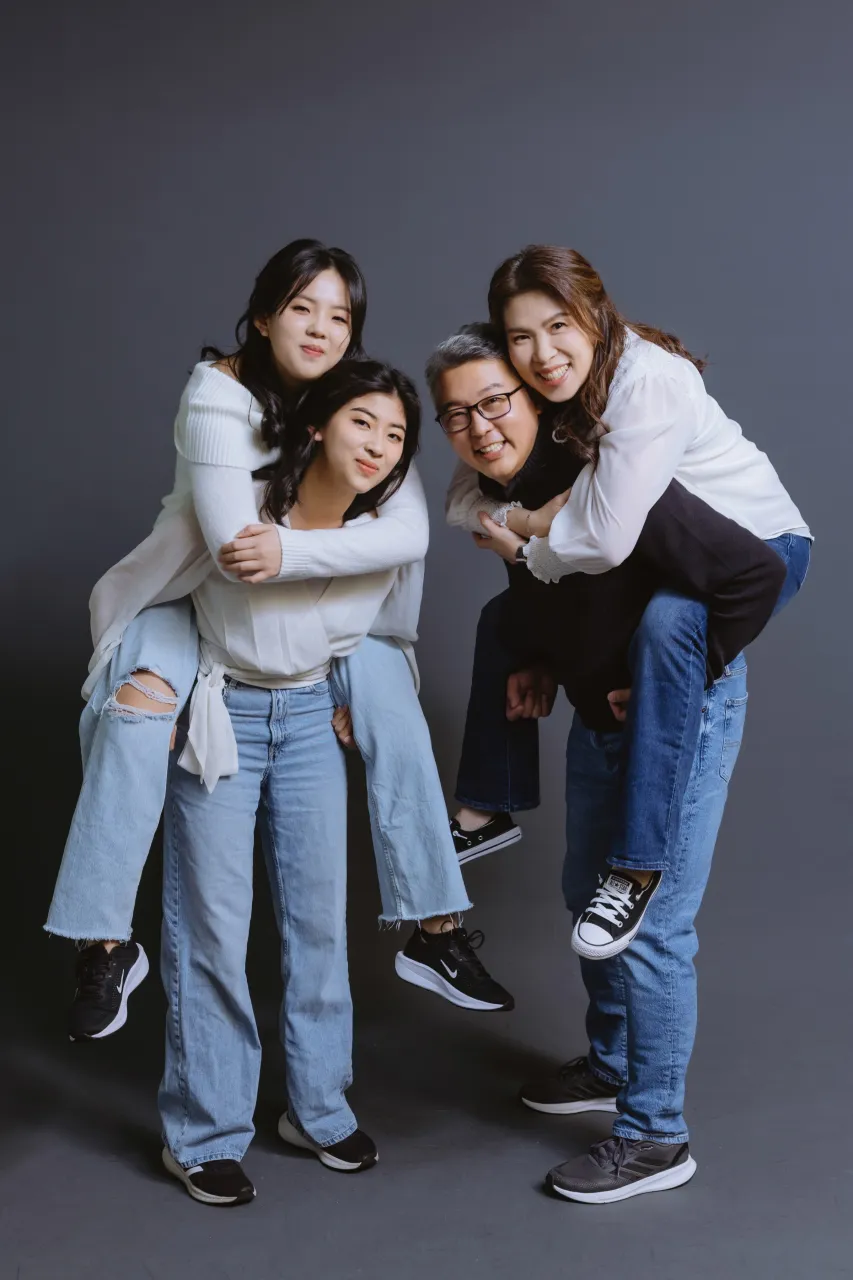 Two piggyback pairs in jeans and white shirts, laughing against a dark backdrop