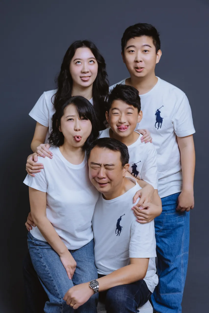 A family in white T-shirts and jeans pulling funny faces together in the studio