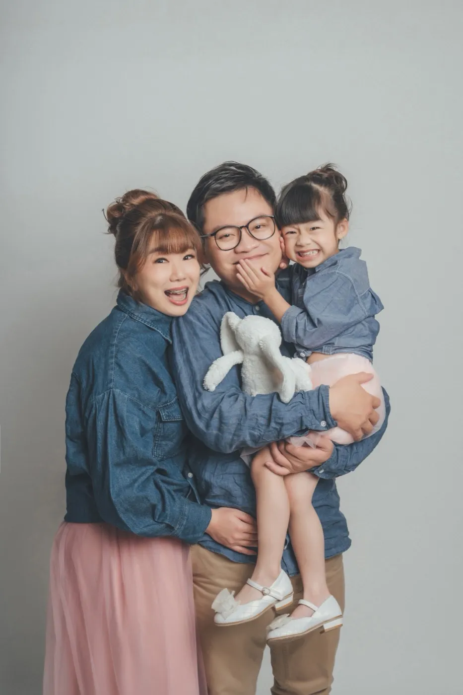 Mum, dad and their daughter in matching denim and chambray, laughing together against a grey backdrop