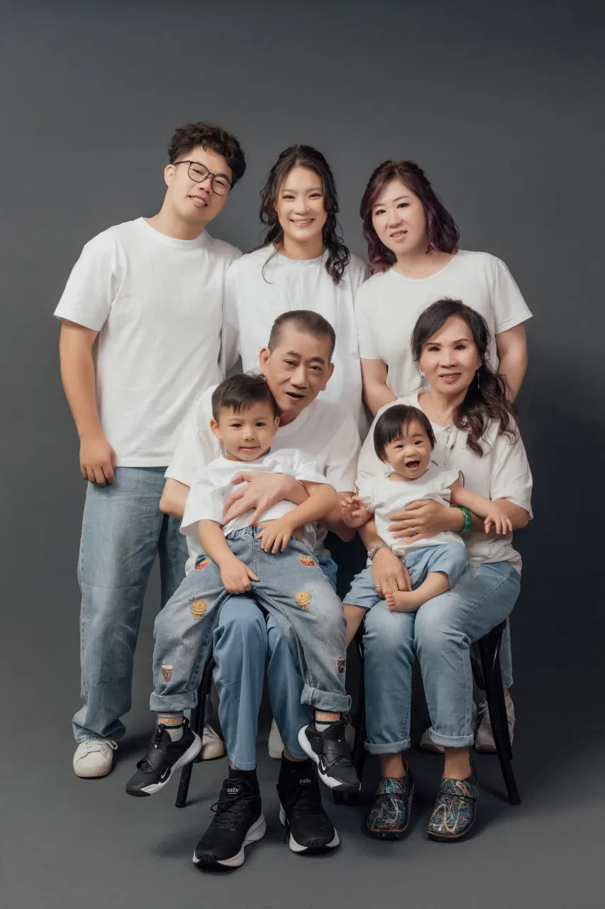 Three generations in white T-shirts and jeans, the grandparents seated with two toddlers on their laps