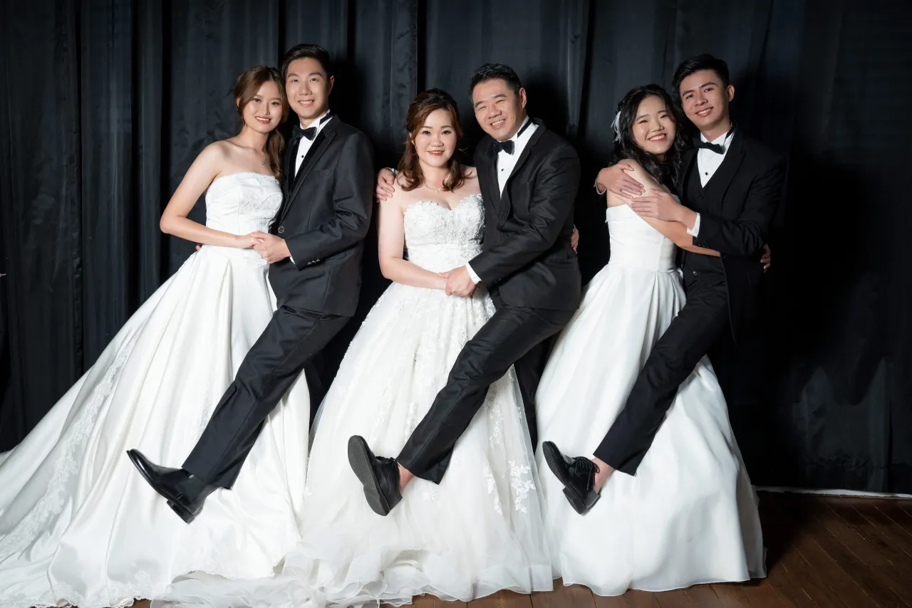 Three couples in tuxedos and white gowns, each pair kicking one leg up for the camera
