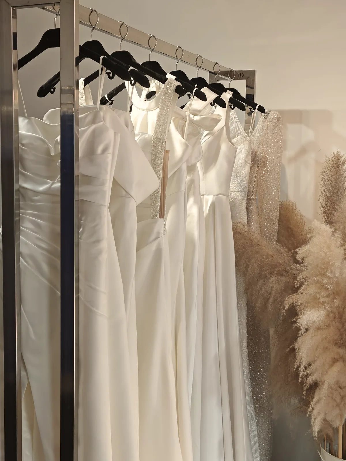 Satin gowns on the boutique rail beside dried pampas grass